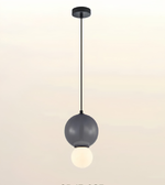A modern pendant light fixture with a matte black ceiling canopy and cord, featuring a large dark gray spherical shade and a smaller glowing white globe bulb underneath, shown against a plain light background.