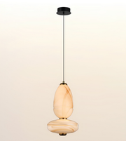 A modern pendant light with a black ceiling canopy and cord, featuring two stacked, organic-shaped glass shades in a warm cream and amber marbled pattern, shown against a light beige gradient background.