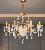 An ornate multi-light chandelier with a warm gold/brass metal frame, clear crystal teardrop pendants, and a frosted glass center bowl, shown hanging in an indoor room setting.