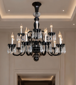 A black multi-arm chandelier with clear crystal droplets and lit candle-style bulbs, hanging in an elegant cream-colored interior hallway.