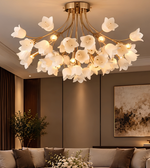 A modern floral ceiling light fixture with white glass flower petals and a gold metal frame, hanging in a contemporary living room with warm ambient lighting.