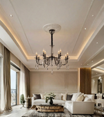Luxury black crystal chandelier with candle-style lights suspended in an elegant living room with neutral furnishings and warm ambient lighting.