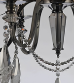 Close-up of a luxury chrome crystal chandelier showing curved metal arms, faceted crystal pendants, and decorative crystal bead garlands.
