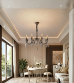 Luxury chrome crystal chandelier with candle-style lights suspended above a dining table in an elegant neutral-toned interior.