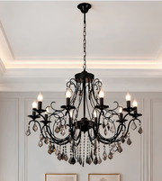 Black luxury chandelier with intricate scrollwork, multiple candle-style bulbs, and hanging crystal accents displayed against a light interior backdrop.
