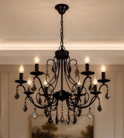 Close-up of a black ornate chandelier featuring curved metal arms, decorative crystal drops, and illuminated candle-shaped bulbs.