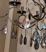Close-up of a black metal chandelier showcasing its curved frame, decorative metalwork, and faceted hanging crystal drops.