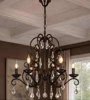 Close-up of a vintage black metal chandelier featuring intricate curved arms, clear crystal droplets, and glowing candle-style bulbs.