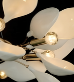 A close-up of a modern multi-arm chandelier with glossy white teardrop-shaped glass shades and brushed brass metal arms, set against a solid black background.