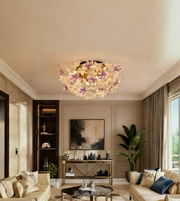 A round ceiling light fixture with a cluster of white and purple artificial flowers, mounted on the ceiling in a modern, beige-toned living room.