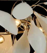 A close-up of a modern chandelier with teardrop-shaped frosted white glass shades and a polished gold-toned metal frame, illuminated against a dark background.