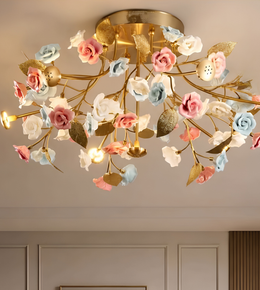 A decorative ceiling light fixture with a gold branch-like frame and multiple faux flowers in pink, white, and light blue, shown installed on a beige ceiling in an indoor room.