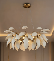 A modern leaf-shaped pendant chandelier with white glass leaf-like shades and a gold metal frame, hanging from a gold ceiling canopy in a warm, dimly lit interior.