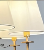 Close-up of a table lamp with a tapered off-white fabric shade and a brushed gold metal base, shown against a pale blue background with a partial text label pointing to the metal base.
