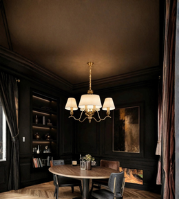 A brass multi-arm chandelier with white drum shades hangs over a round wooden dining table in a dark, elegant room with black paneled walls and built-in shelves.