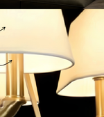 Close-up of a luxury gold chandelier with five ivory tapered shades, curved metal arms, and decorative central detailing.
Copy alt text