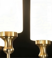 Close-up of two brass candlestick holders or lamp bases in front of large white rectangular light panels against a dark background.