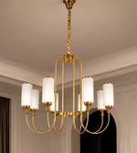 Close-up of a gold eight-light chandelier featuring white cylindrical shades, curved metal arms, and an elongated central frame.
