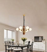 A modern multi-light chandelier with six white spherical glass globes and a warm wood-and-brass-toned central body, hanging in a dining room above a dark table.
