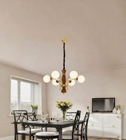 A modern multi-light chandelier with six white spherical glass globes and a warm wood-and-brass-toned central body, hanging in a dining room above a dark table.
