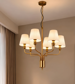 Gold six-light chandelier with cream pleated lampshades and curved metal arms in an elegant modern interior.