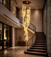 Elongated acrylic flame cascade chandelier in a luxury staircase with warm ambient lighting