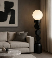 Black sculptural floor lamp with opal globe beside modern sofa in living room