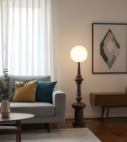 Wooden finish sculptural floor lamp with opal globe beside sofa in living room