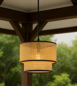 Woven outdoor pendant light hanging under a wooden pergola with greenery in the background