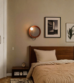 Modern circular wall sconce with wooden frame installed above bed