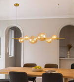 Modern amber glass globe chandelier with gold frame hanging above dining table with warm ambient lighting