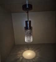 Modern pendant light fixture with textured glass shade in a dimly lit room.
