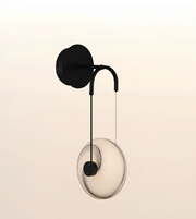 Modern wall-mounted light fixture with a matte black circular wall plate, curved arm, and a large oval translucent glass shade, shown against a soft warm beige gradient background.