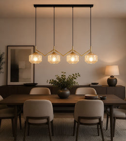 A modern 4-light linear pendant chandelier with textured glass globes and gold-toned geometric arms, hanging over a dining table in a warm, contemporary dining room setting.