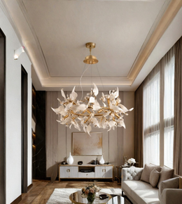 A large, modern chandelier with white sculptural leaf-like petals and gold metal accents hangs in a luxurious, high-ceilinged living room with beige walls, a tufted sofa, and large windows.