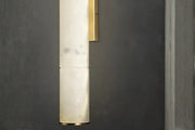 Minimal marble tube wall sconce with brass accents glowing softly