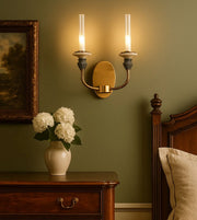 Elegant gold wall sconce with two lights above a wooden nightstand and floral decor
