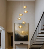 Modern gold pendant chandelier in a high-ceiling foyer with abstract wall art and staircase
