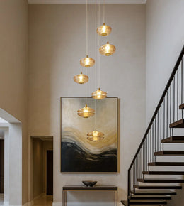 Modern gold pendant chandelier in a high-ceiling foyer with abstract wall art and staircase