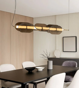 Modern gold linear pendant light over black dining table with minimalist decor