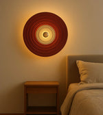 Modern circular wall sconce with layered rings, warm light above wooden bedside table