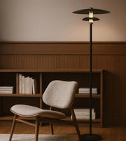 Modern floor lamp next to a chair and bookshelf in a room with wooden paneling.